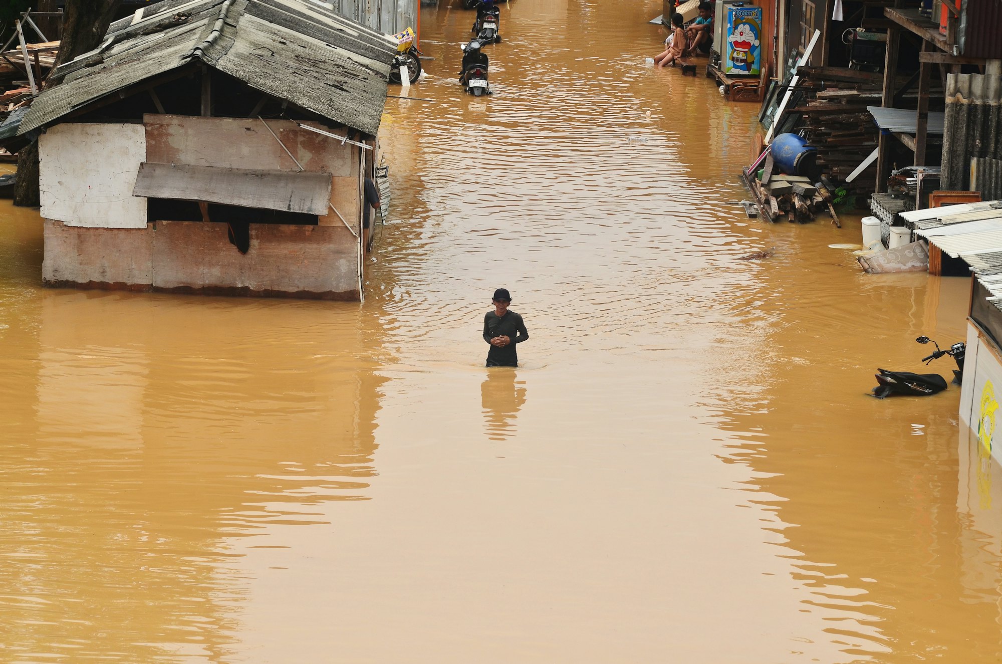 Una persona camina con el agua a la cintura por una calle inundada entre casas de lámina